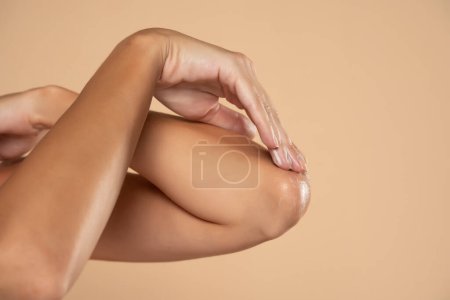 Téléchargez les photos : Gros plan d'une femme prend soin de ses coudes en utilisant de la crème cosmétique sur un fond de studio beige - en image libre de droit