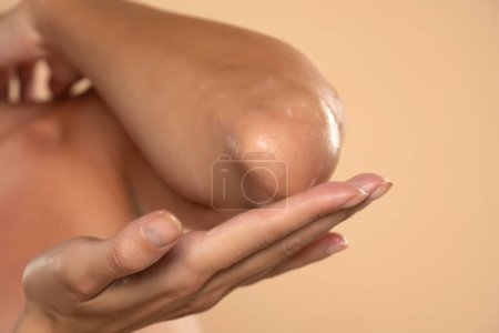 Photo for Close-up of a woman takes care of his elbows using cosmetic cream on a beige studio background - Royalty Free Image