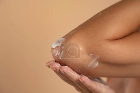 Foto de Primer plano de una mujer se encarga de sus codos usando crema cosmética en un fondo de estudio beige - Imagen libre de derechos