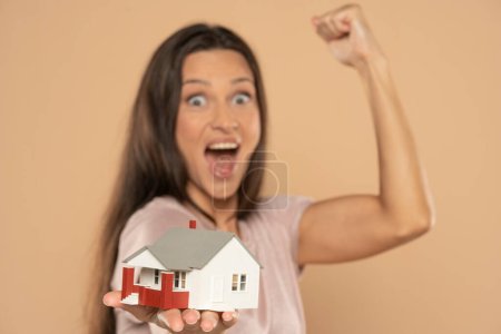 Foto de Young happy  woman holding house sample model isolated over beige studio background, Real estate and home insurance concept - Imagen libre de derechos