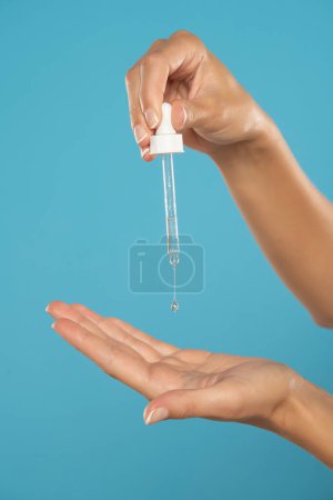 Téléchargez les photos : Woman holds glass pipette with natural essential oil or organic serum. Moisturizing oil is dropping on hand's skin from pipette. Concept of home body care and healthy lifestyle. - en image libre de droit