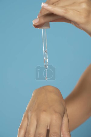 Foto de Woman holds glass pipette with natural essential oil or organic serum. Moisturizing oil is dropping on hand's skin from pipette. Concept of home body care and healthy lifestyle. - Imagen libre de derechos