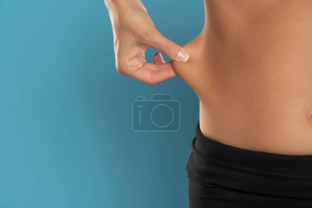 Téléchargez les photos : Closeup of a young fit woman pinching her waist skin on a blue studio background - en image libre de droit