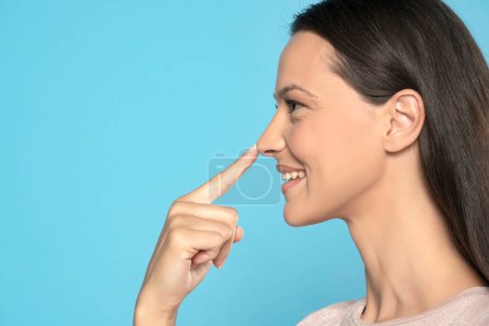 Profile of young smiling woman touching her nose on a blue studio background