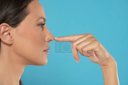Foto de Perfil de una mujer joven tocándose la nariz sobre un fondo azul de estudio - Imagen libre de derechos