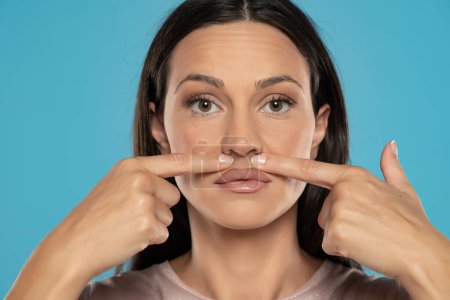 Téléchargez les photos : Femme touche son visage sous son nez sur un fond bleu studio - en image libre de droit