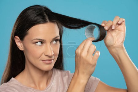 Téléchargez les photos : Young woman putting curlers in her hair on a blue studio background - en image libre de droit