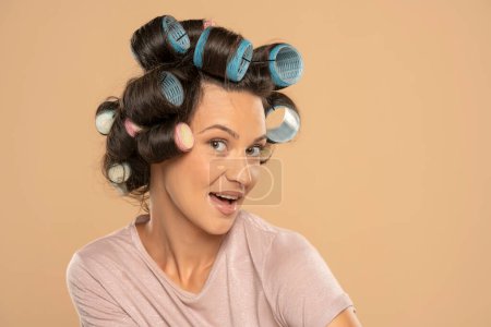Téléchargez les photos : Beautiful smiling woman with hair curlers posing on a beige studio  background - en image libre de droit