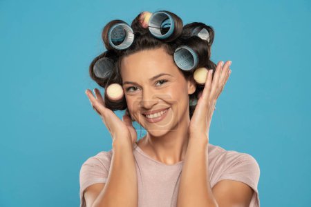 Foto de Hermosa mujer sonriente con rizadores de pelo posando sobre un fondo de estudio azul - Imagen libre de derechos