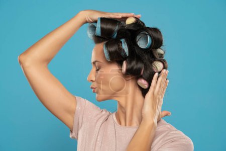 Téléchargez les photos : Beautiful smiling woman with hair curlers posing on a blue studio  background. Profile view. - en image libre de droit