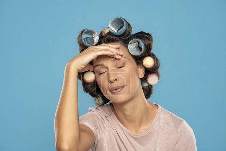 Téléchargez les photos : Beautiful bored woman with hair curlers on a blue studio  background - en image libre de droit