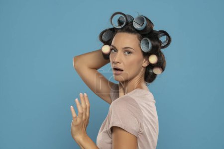 Photo for Beautiful woman with hair curlers posing on a blue studio  background - Royalty Free Image