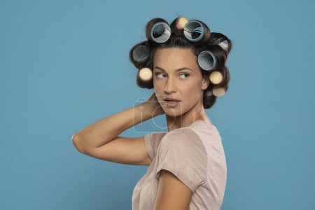 Téléchargez les photos : Beautiful woman with hair curlers posing on a blue studio  background - en image libre de droit