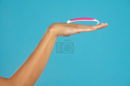 Téléchargez les photos : A female hand holds a disposable pink razor on a blue studio background - en image libre de droit