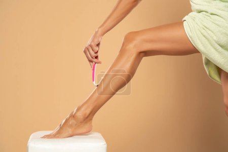 Téléchargez les photos : Woman shaves her legs on beige studio background - en image libre de droit