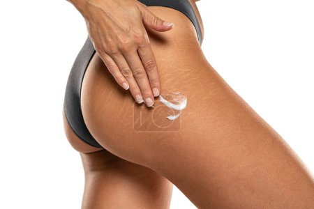 Photo for Woman applying stretch marks lotion on her hips on a white studio background - Royalty Free Image