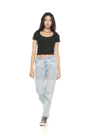 Photo for Young beautiful woman in loose jeans walking on white studio background - Royalty Free Image