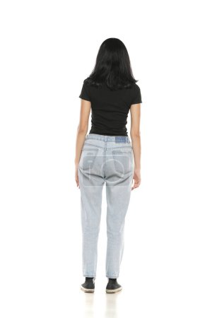 Photo for Back view of a young woman in loose jeans posing on white studio background - Royalty Free Image