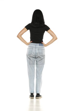 Téléchargez les photos : Back view of a young woman in loose jeans posing on white studio background - en image libre de droit
