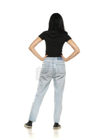 Foto de Back view of a young woman in loose jeans posing on white studio background - Imagen libre de derechos