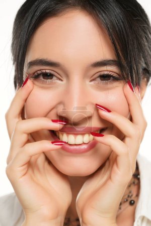Foto de Una mujer feliz muestra su esmalte de uñas rojo sobre un fondo de estudio blanco. de cerca - Imagen libre de derechos