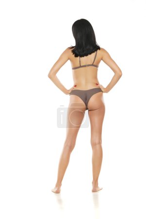 Photo for Back view of a young brunette woman in bikini swimsuit posing on a white studio  background. - Royalty Free Image