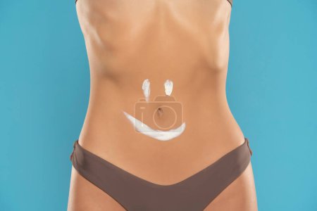 Photo for Woman's belly close-up with smile drawn with lotion on a blue studio background - Royalty Free Image