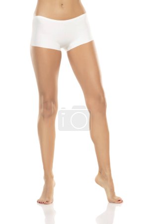 Foto de Front view of female barefoot legs in white bikini panties on a white studio background. - Imagen libre de derechos