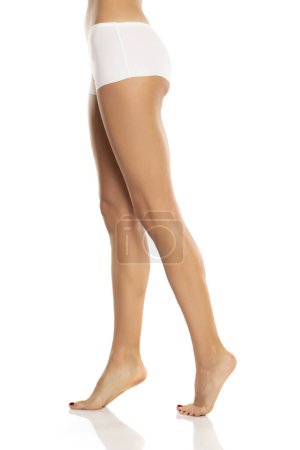 Téléchargez les photos : Vue latérale des jambes nues féminines en culotte de bikini blanche sur fond de studio blanc. - en image libre de droit