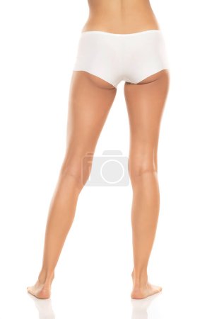 Téléchargez les photos : Vue arrière des jambes nues féminines en culotte de bikini blanche sur fond de studio blanc. - en image libre de droit