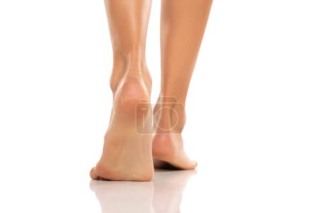 Téléchargez les photos : Vue arrière d'une femme joliment soignée pieds nus sur un fond de studio blanc. - en image libre de droit