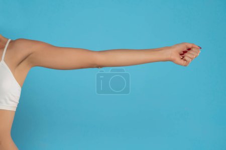 Téléchargez les photos : Young woman's stretched arm and fist. Isolated on blue studio background. - en image libre de droit