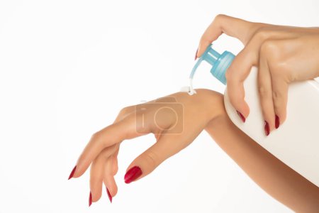 Téléchargez les photos : Une femme applique un produit cosmétique avec une pompe à la main sur un fond de studio blanc - en image libre de droit