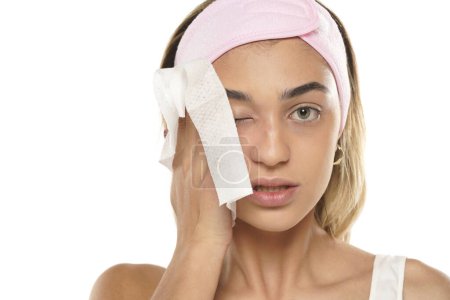 Téléchargez les photos : Jolie jeune femme qui nettoie son visage avec un mouchoir sur fond de studio blanc - en image libre de droit