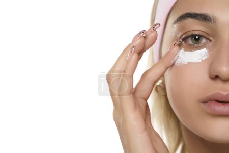 Foto de Belleza mujer joven aplicando crema cosmética bajo sus ojos en un fondo de estudio blanco - Imagen libre de derechos