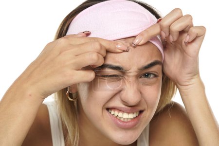 Téléchargez les photos : Nerveux jeune femme serrant des boutons sur son visage sur fond de studio blanc - en image libre de droit