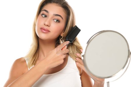 Téléchargez les photos : Jeune femme brossant des cheveux sains devant un miroir sur un fond de studio blanc - en image libre de droit