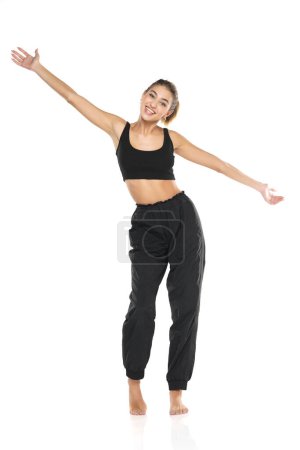Photo for A young barefeet happy woman in black sweatpants and a tank top on a white studio background - Royalty Free Image