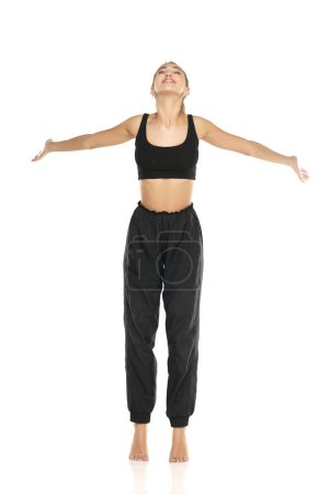 Photo for A young barefeet happy woman in black sweatpants and a tank top on a white studio background - Royalty Free Image