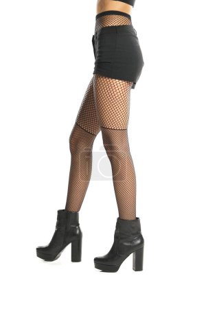 Photo for Young female legs in black fishnet stockings shorts, nad leather boots on white studio background. Side, profile view - Royalty Free Image