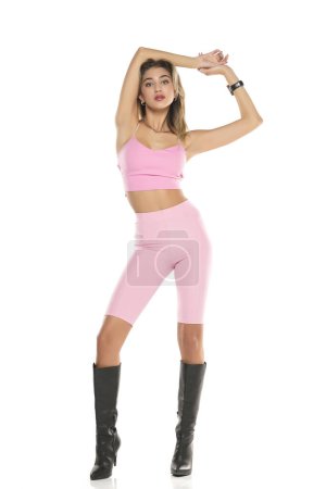 Téléchargez les photos : Une jeune femme en legging court rose et haut, et des bottes en cuir noir sur fond de studio blanc - en image libre de droit