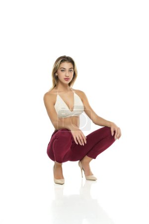 Photo for A young woman in burgundy jeans and top, and high heels shoes posing on a white studio background - Royalty Free Image