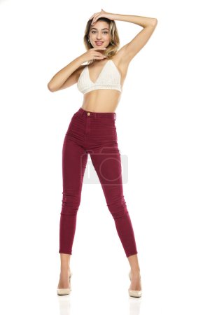 Photo for A young woman in burgundy jeans and top, and high heels shoes posing on a white studio background - Royalty Free Image