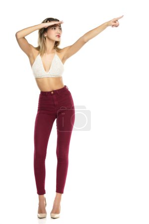 Photo for Smiling Woman In Burgundy Jeans And Top Presenting Something ,Touching, Showing Direction On A White Studio Background - Royalty Free Image