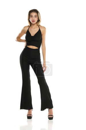 Téléchargez les photos : Une jeune femme en pantalon large noir et soutien-gorge posant sur un fond de studio blanc - en image libre de droit