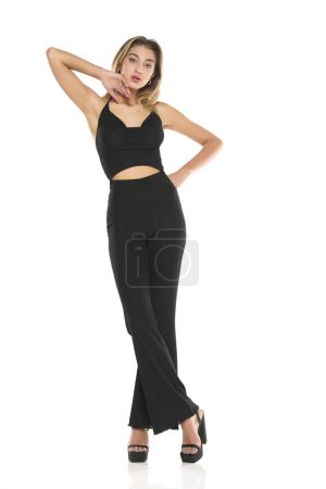 Téléchargez les photos : Une jeune femme en pantalon large noir et soutien-gorge posant sur un fond de studio blanc - en image libre de droit