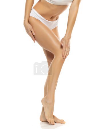 Téléchargez les photos : Plan studio d'une femme méconnaissable touchant ses jolies jambes sur fond de studio blanc - en image libre de droit