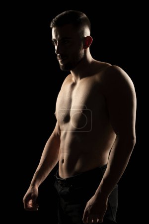 Photo for Silhouette of a muscular shirtless man in the shadow on a black studio background - Royalty Free Image