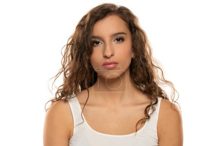 Téléchargez les photos : Portrait d'une jeune femme sérieuse avec maquillage et longs cheveux ondulés sur fond de studio blanc - en image libre de droit
