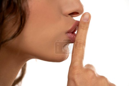 Photo for Cropped image of a young woman holding index finger at her lips, saying 'shh' on a white studio background. side profile view - Royalty Free Image